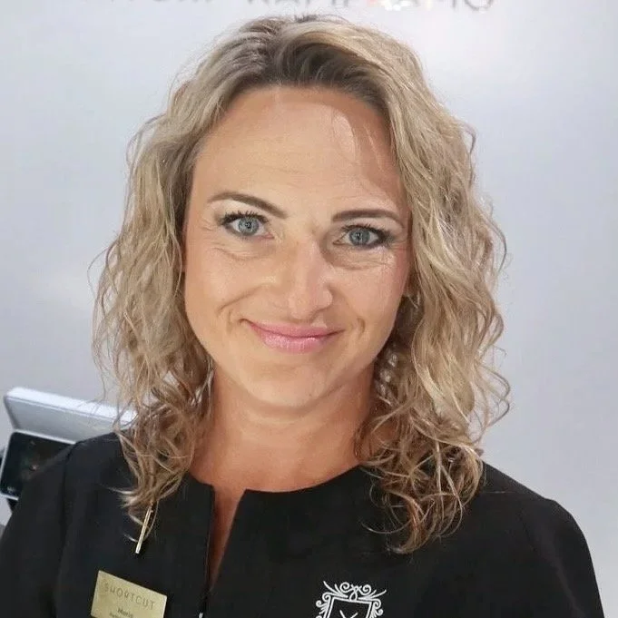 Naispuolinen nainen puserossa ja korussa, kuvassa on harmaa tausta. Parturi-kampaaja Maria R, Shortcut STOCKMANN