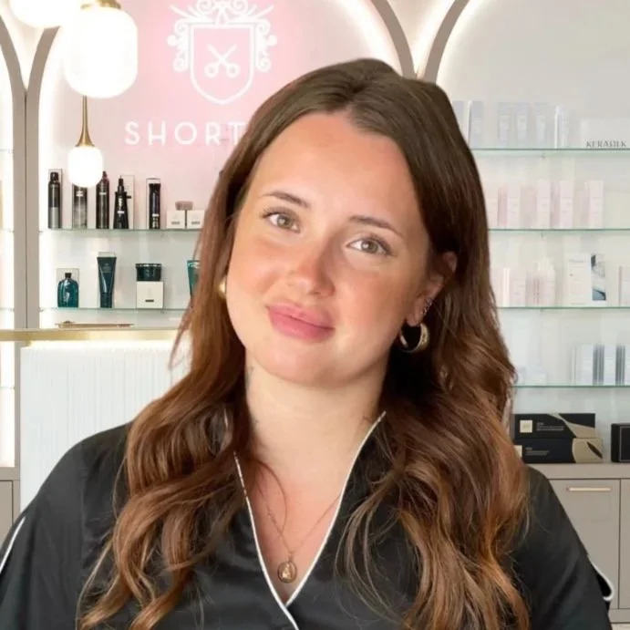 Nuori nainen, ruskeat hiukset, korvakorut, hymy, yrittäjä tai ammattilainen, toimistoympäristö. Parturi-kampaaja Veera, Shortcut AALTO