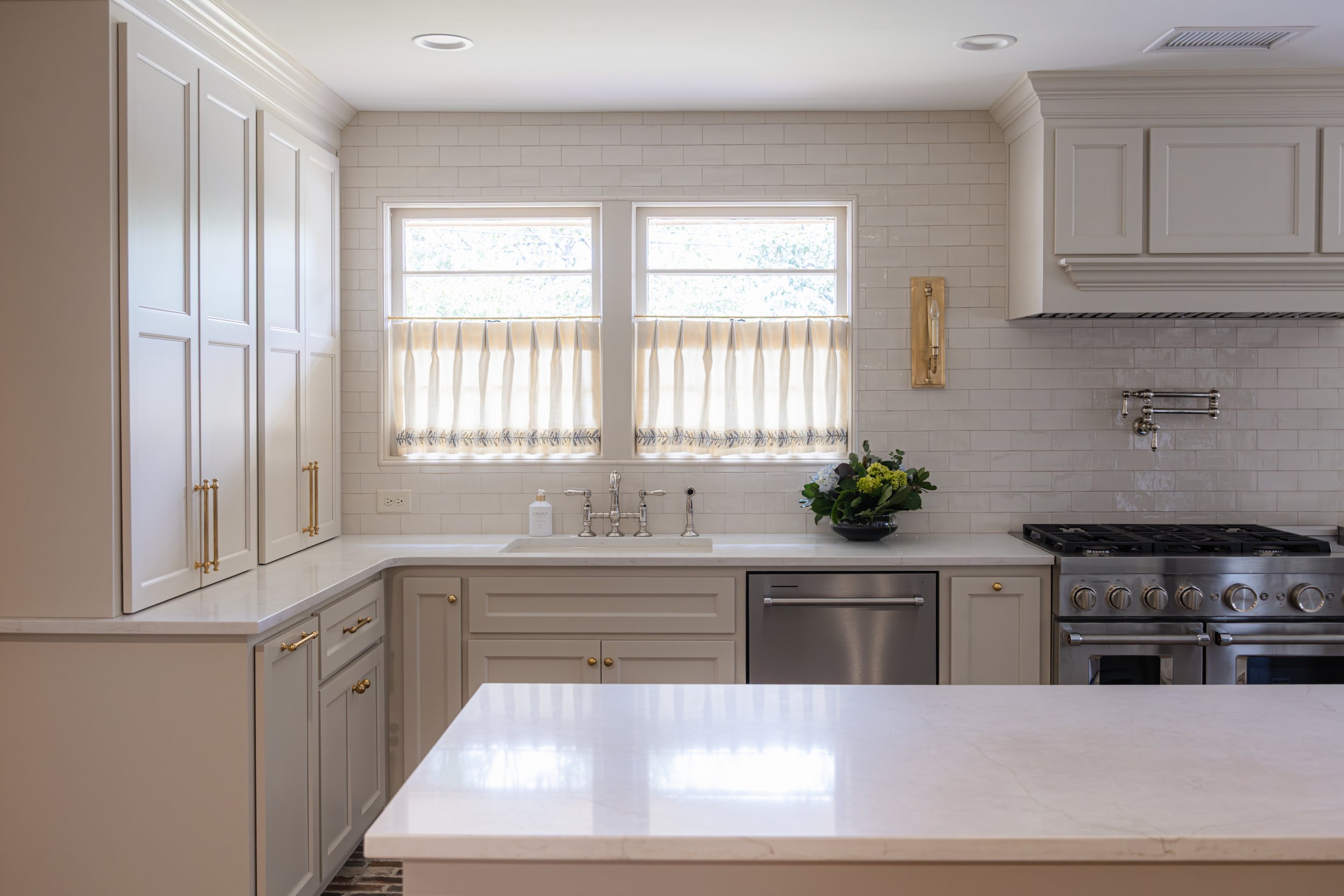 Bright kitchen with white cabinets, quartz countertop island, stainless steel range, and a double window above the sink letting in natural light.