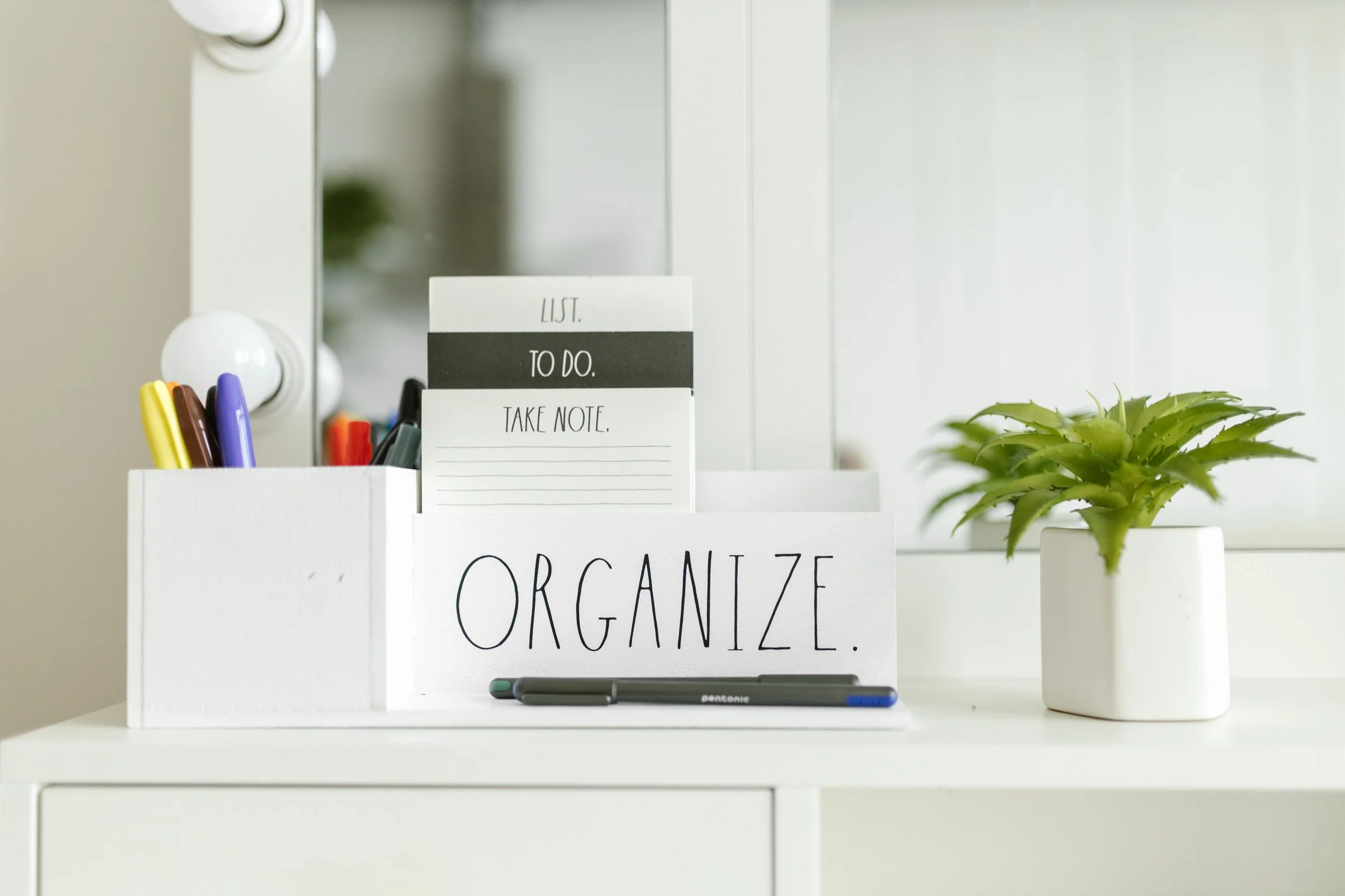An organized desk with pens and a notepad inside a box that says ORGANIZE.