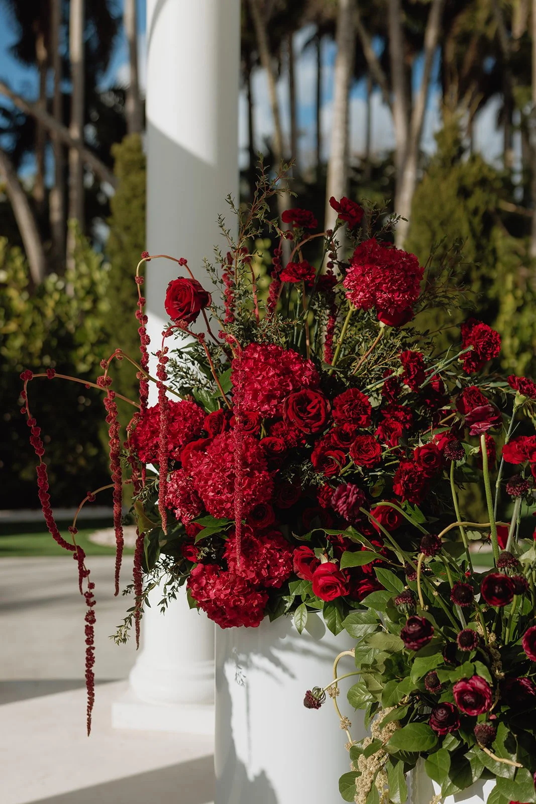Luxury outdoor wedding ceremony featuring elegant red floral pedestal arrangements beneath a white gazebo, designed by Atico Floral, a Miami and South Florida wedding florist.