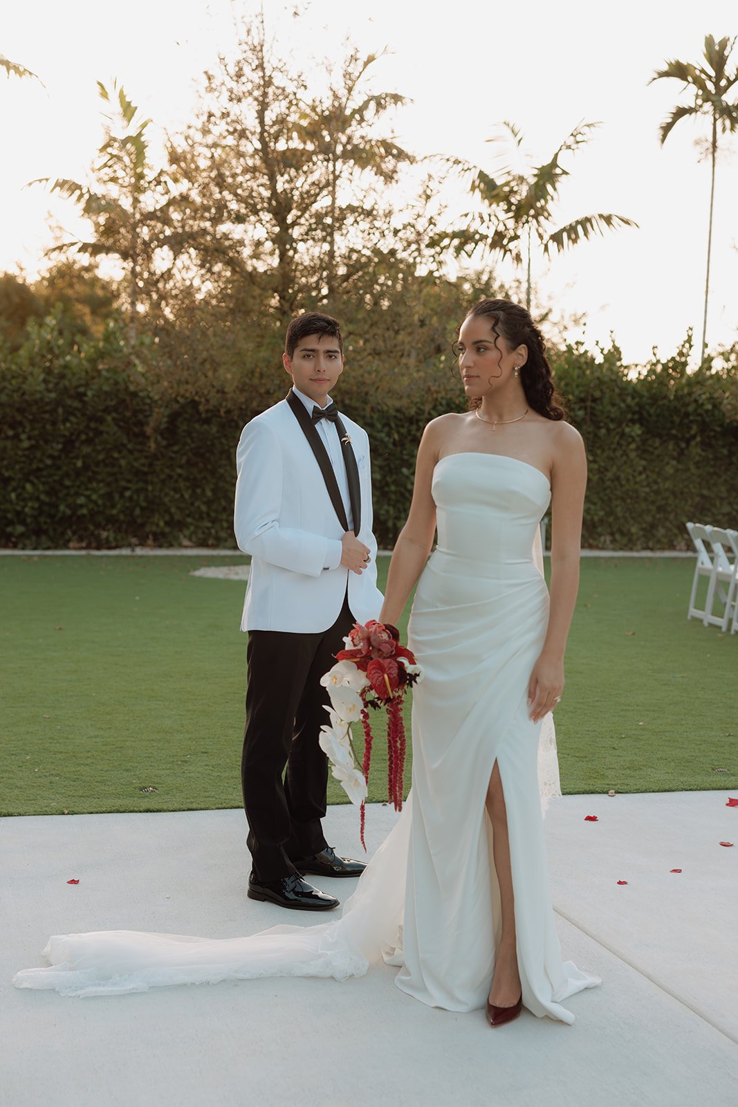 Elegant bride and groom sharing a kiss while showcasing a dramatic cascading bridal bouquet with white orchids and crimson roses at a luxury Florida wedding.