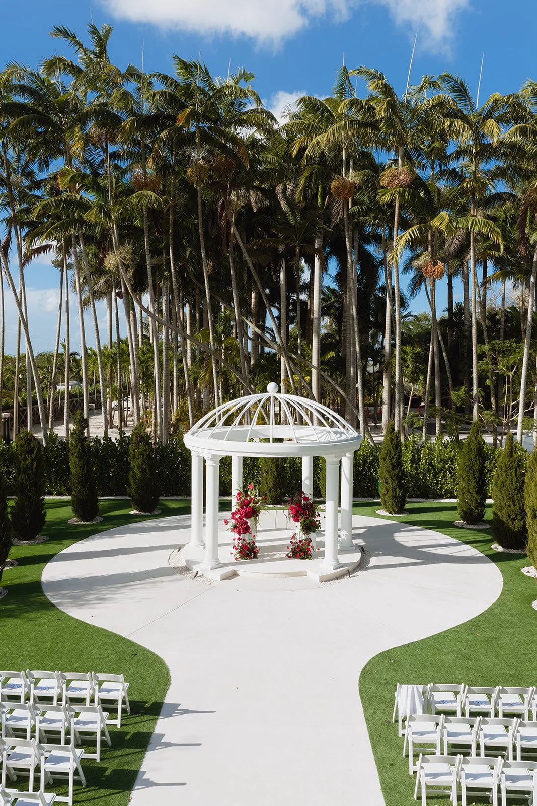 Looking for luxury wedding ceremony inspiration? This elegant white gazebo is adorned with lush red floral arrangements featuring premium roses, orchids, and cascading accents to create a romantic outdoor wedding ceremony in South Florida.
