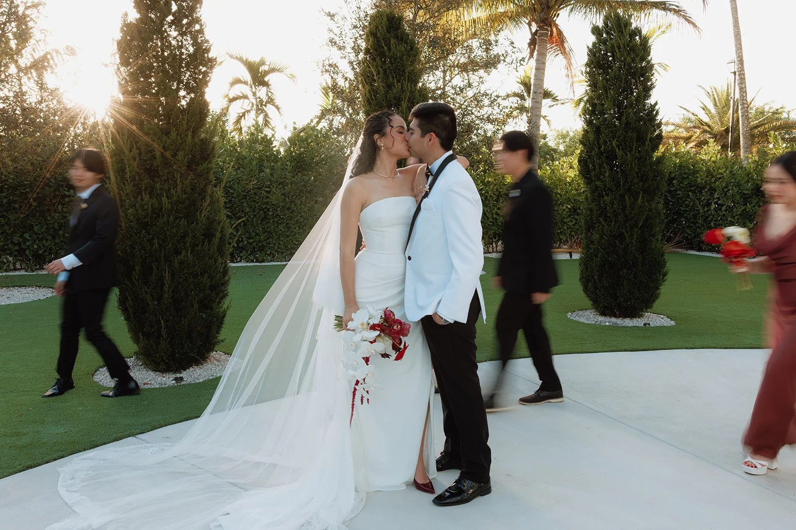 Elegant bride and groom sharing a kiss while showcasing a dramatic cascading bridal bouquet with white orchids and crimson roses at a luxury Florida wedding.