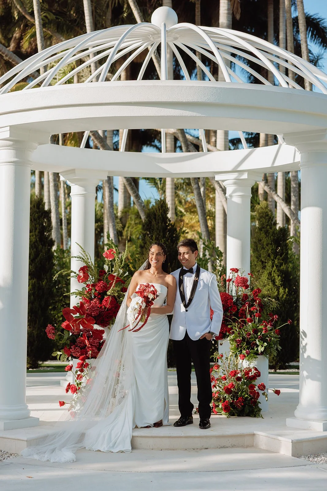 Bold, romantic ceremony florals designed beneath a classic white gazebo, featuring lush red roses, orchids, and cascading blooms. Atico Floral creates luxury wedding ceremony designs throughout Miami, Palm Beach, and South Florida, transforming beaut