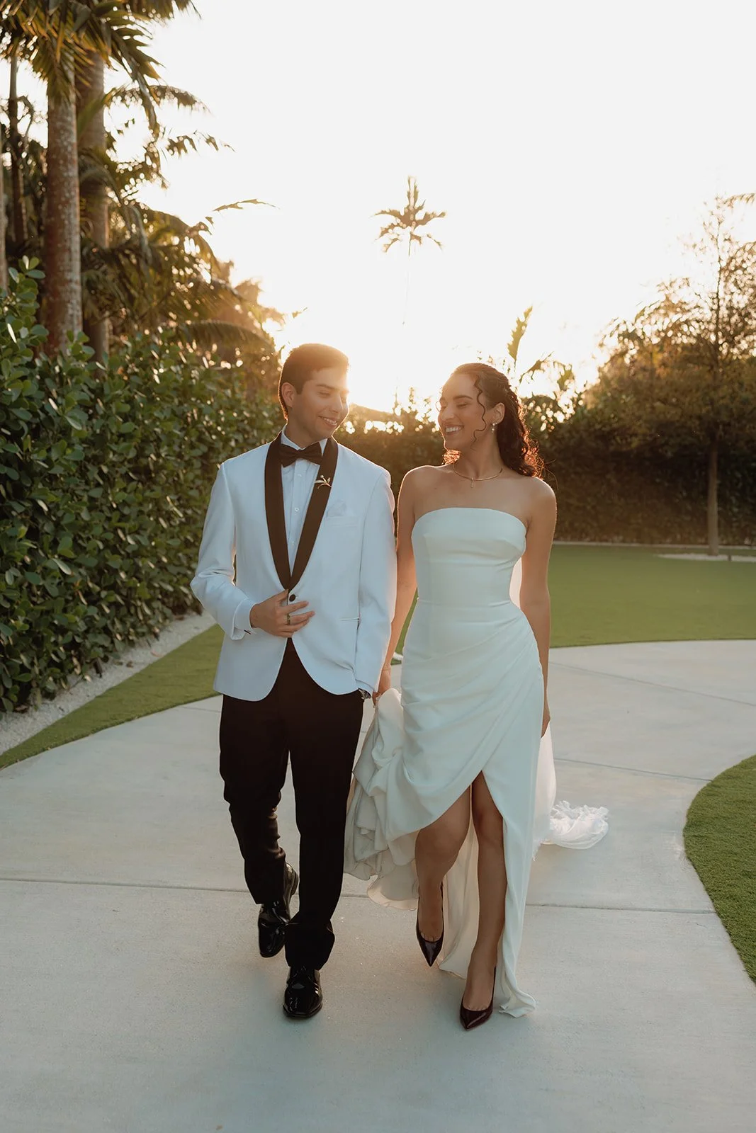 Bride and groom sharing a kiss during sunset while holding a cascading orchid and red rose bridal bouquet designed by Atico Floral, a luxury South Florida wedding florist.