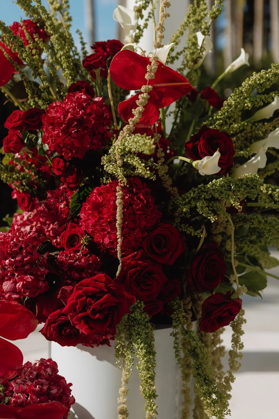 Luxury outdoor wedding ceremony featuring elegant red floral pedestal arrangements beneath a white gazebo, designed by Atico Floral, a Miami and South Florida wedding florist.
