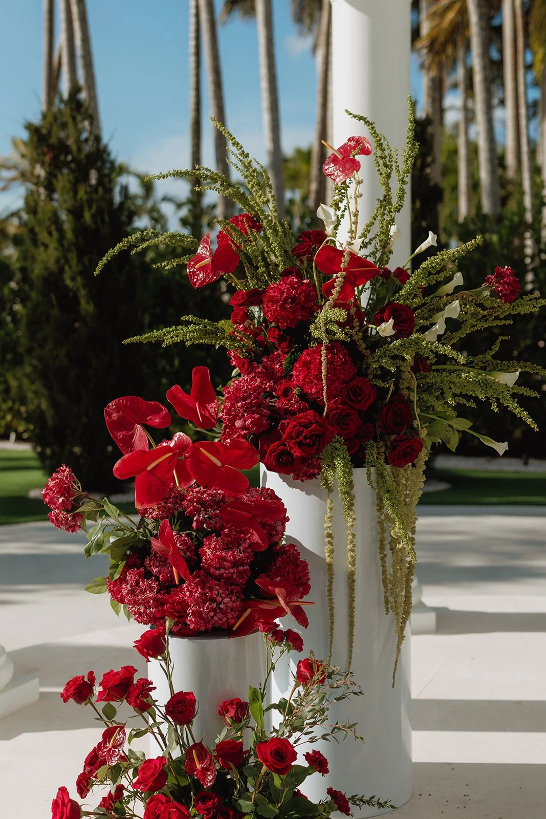 Luxury outdoor wedding ceremony featuring elegant red floral pedestal arrangements beneath a white gazebo, designed by Atico Floral, a Miami and South Florida wedding florist.