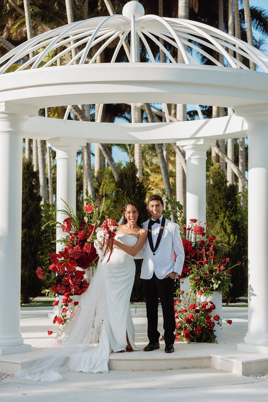 Bold, romantic ceremony florals designed beneath a classic white gazebo, featuring lush red roses, orchids, and cascading blooms. Atico Floral creates luxury wedding ceremony designs throughout Miami, Palm Beach, and South Florida, transforming beaut