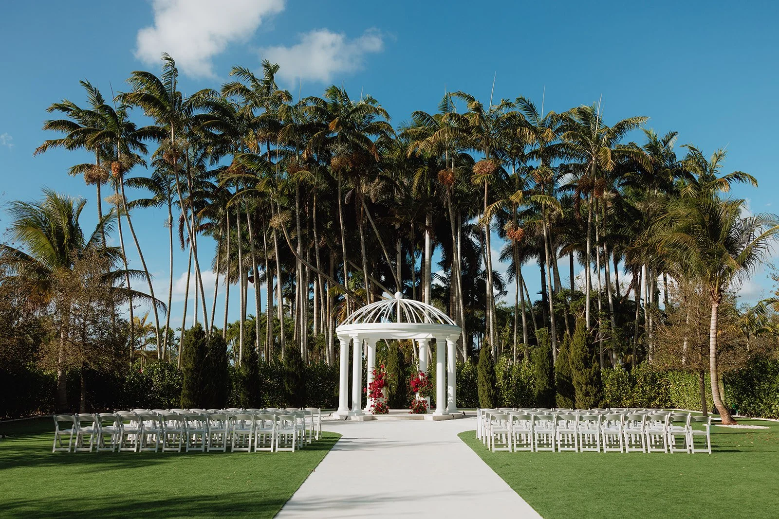 Looking for luxury wedding ceremony inspiration? This elegant white gazebo is adorned with lush red floral arrangements featuring premium roses, orchids, and cascading accents to create a romantic outdoor wedding ceremony in South Florida.
