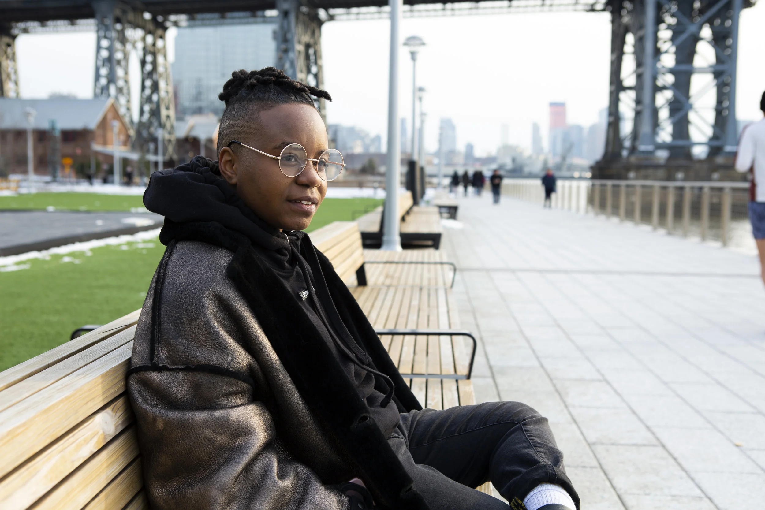 A transmasculine person sitting in a park and smiling