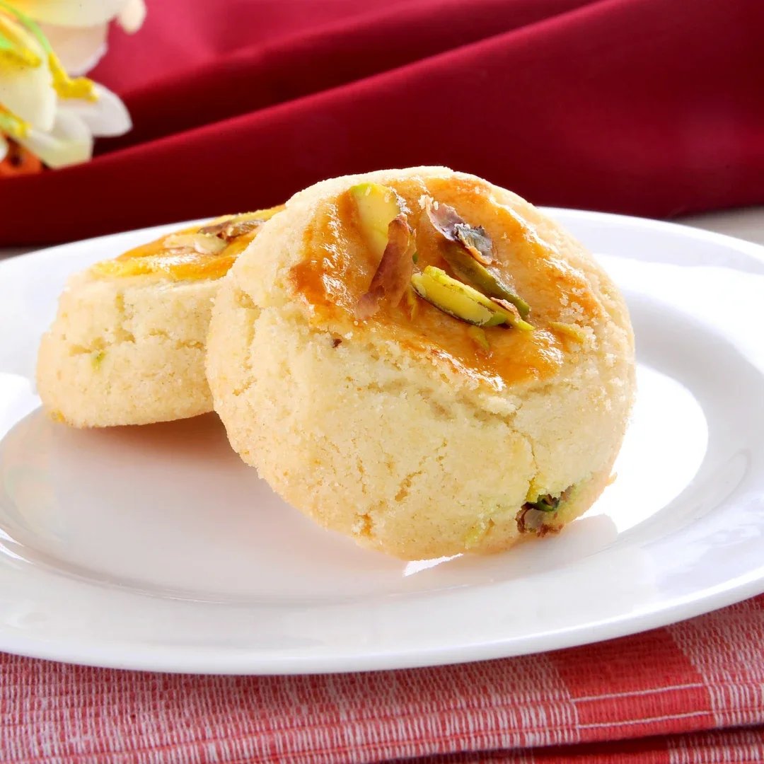 Two round Indian sweet ladoos garnished with chopped pistachios and saffron saffron shavings on a white plate.