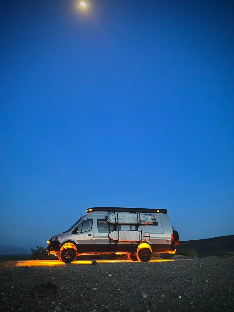 EAV Wolf Adventure Van at night with surfboards strapped to the side and under glow turned on.