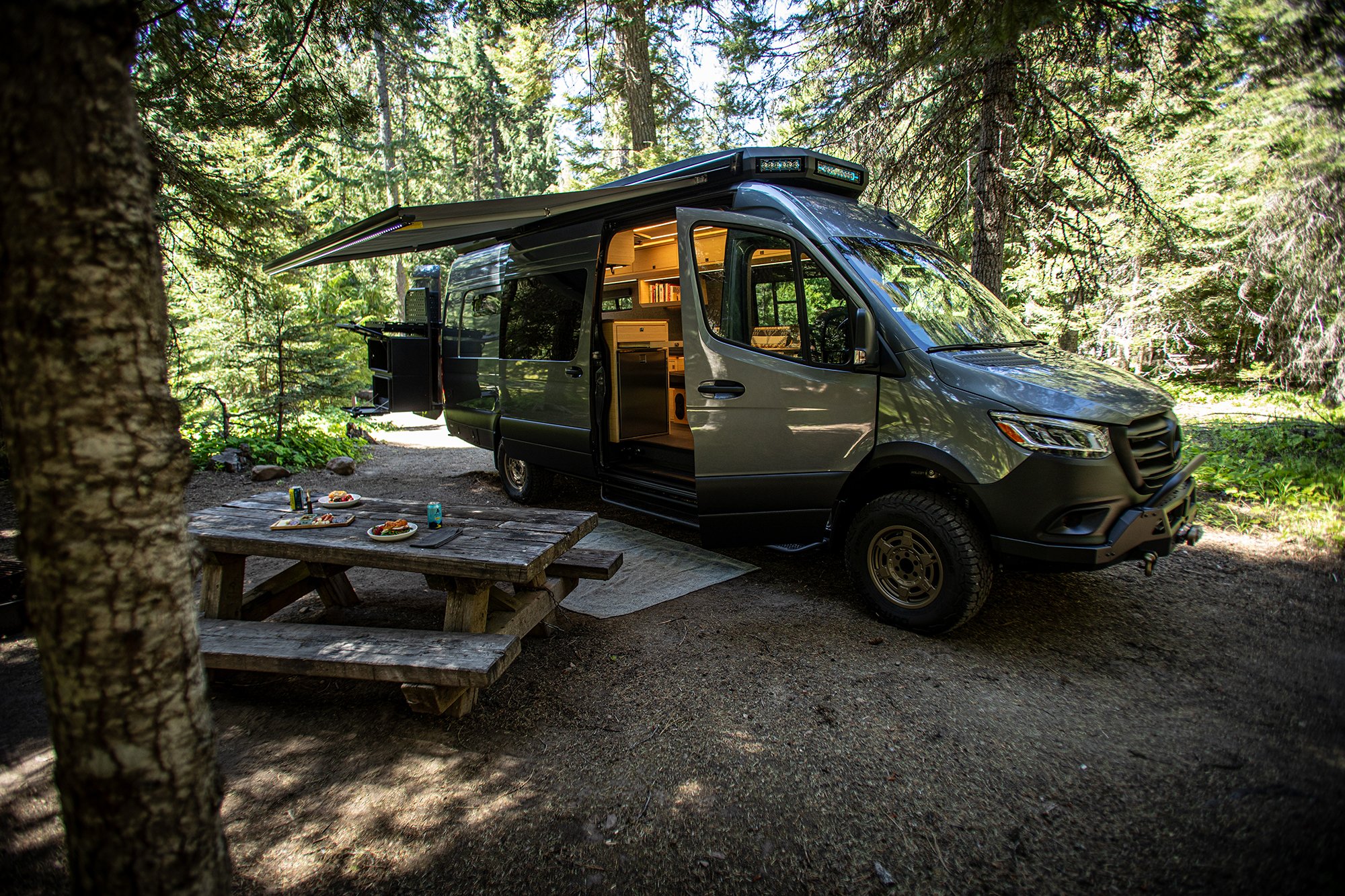 EAV Earl Grey adventure van with awning out and a picnic table setup next to it.