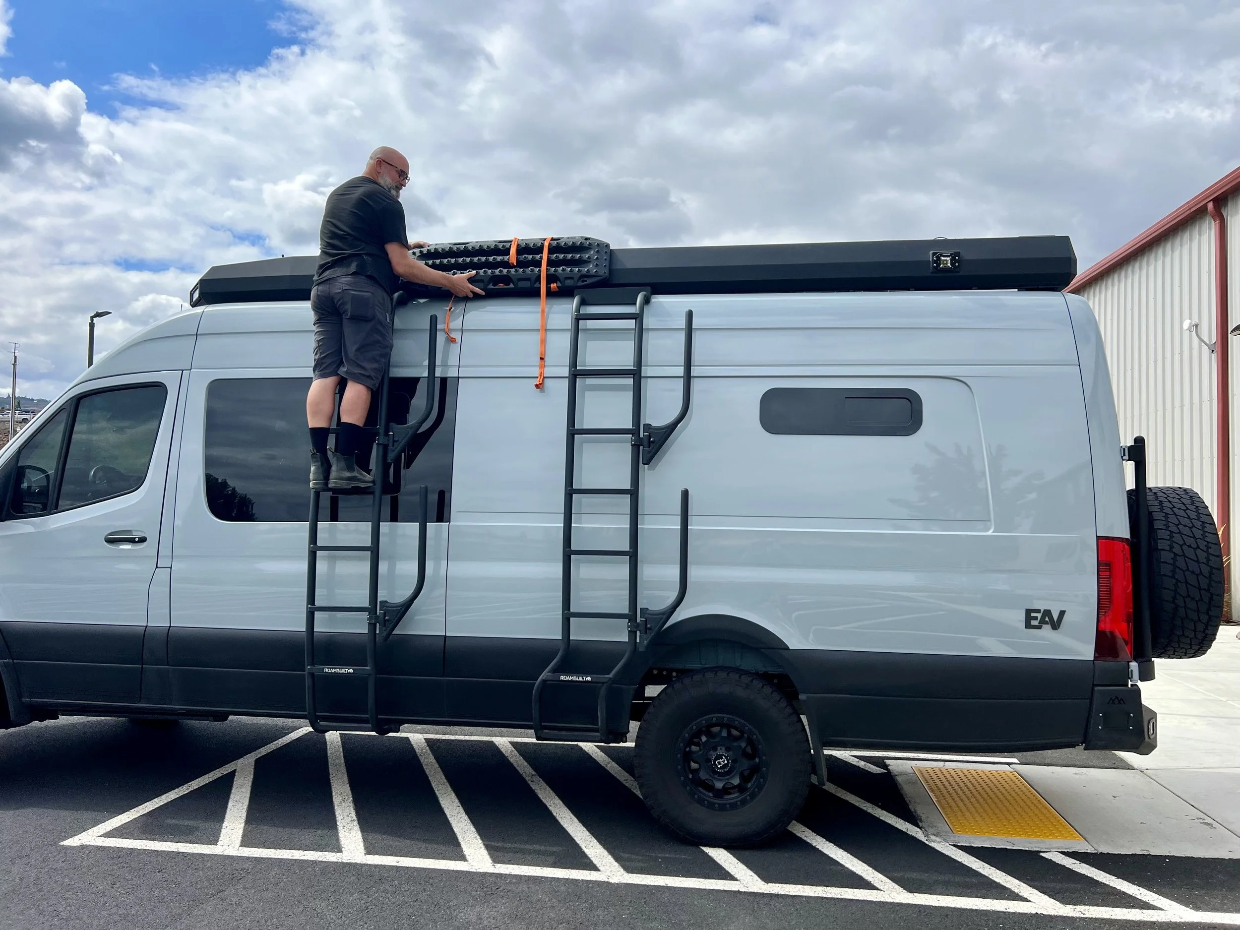 A man strapping something to EAV Wolf Adventure Van's roof.