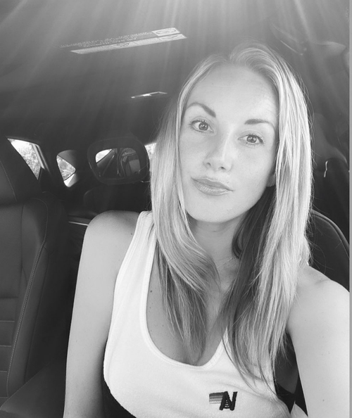 A young woman with long hair taking a selfie inside a car, sitting in the passenger seat.