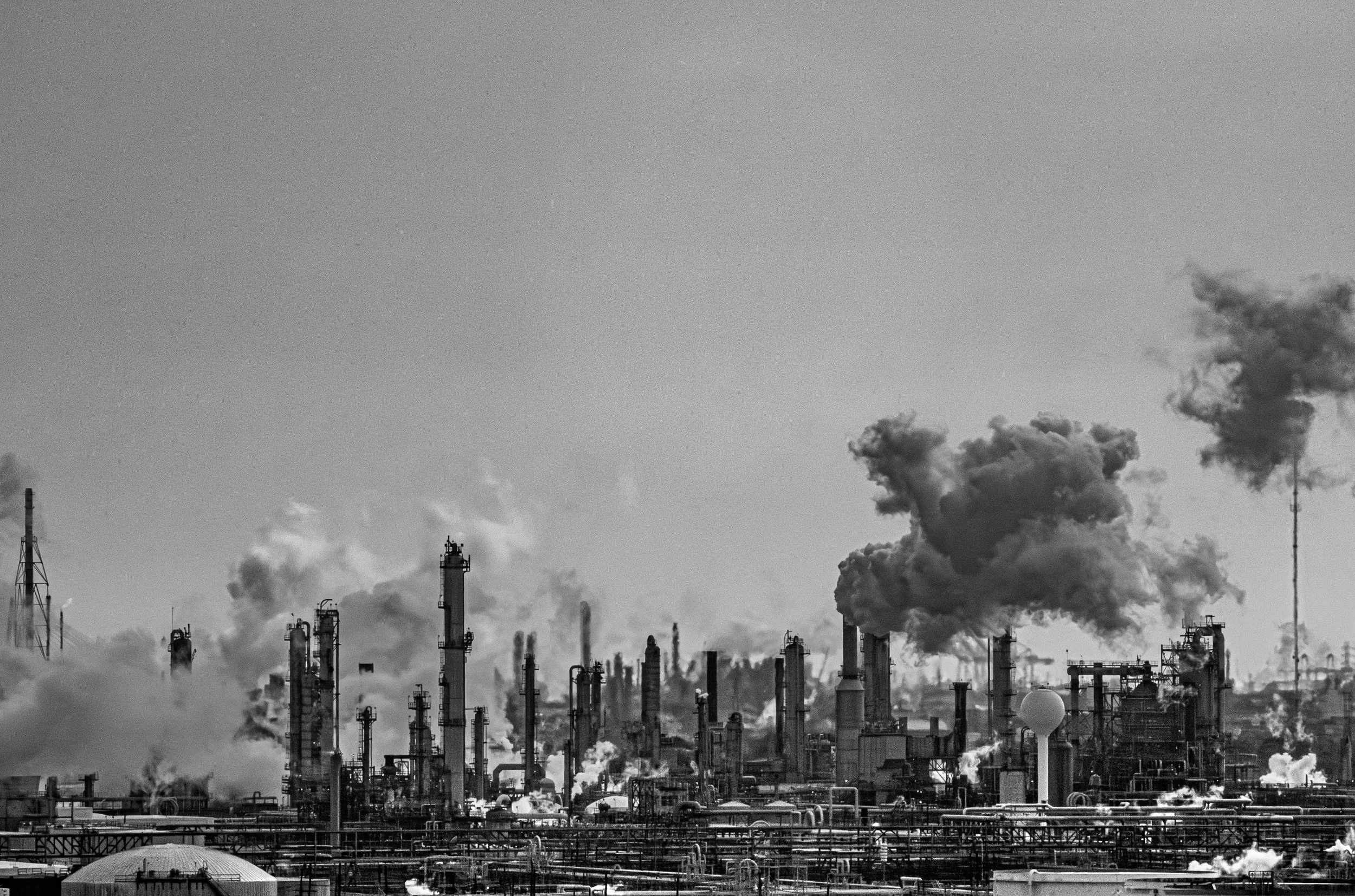 Black and white photo of an industrial factory with multiple smokestacks emitting smoke into the sky.