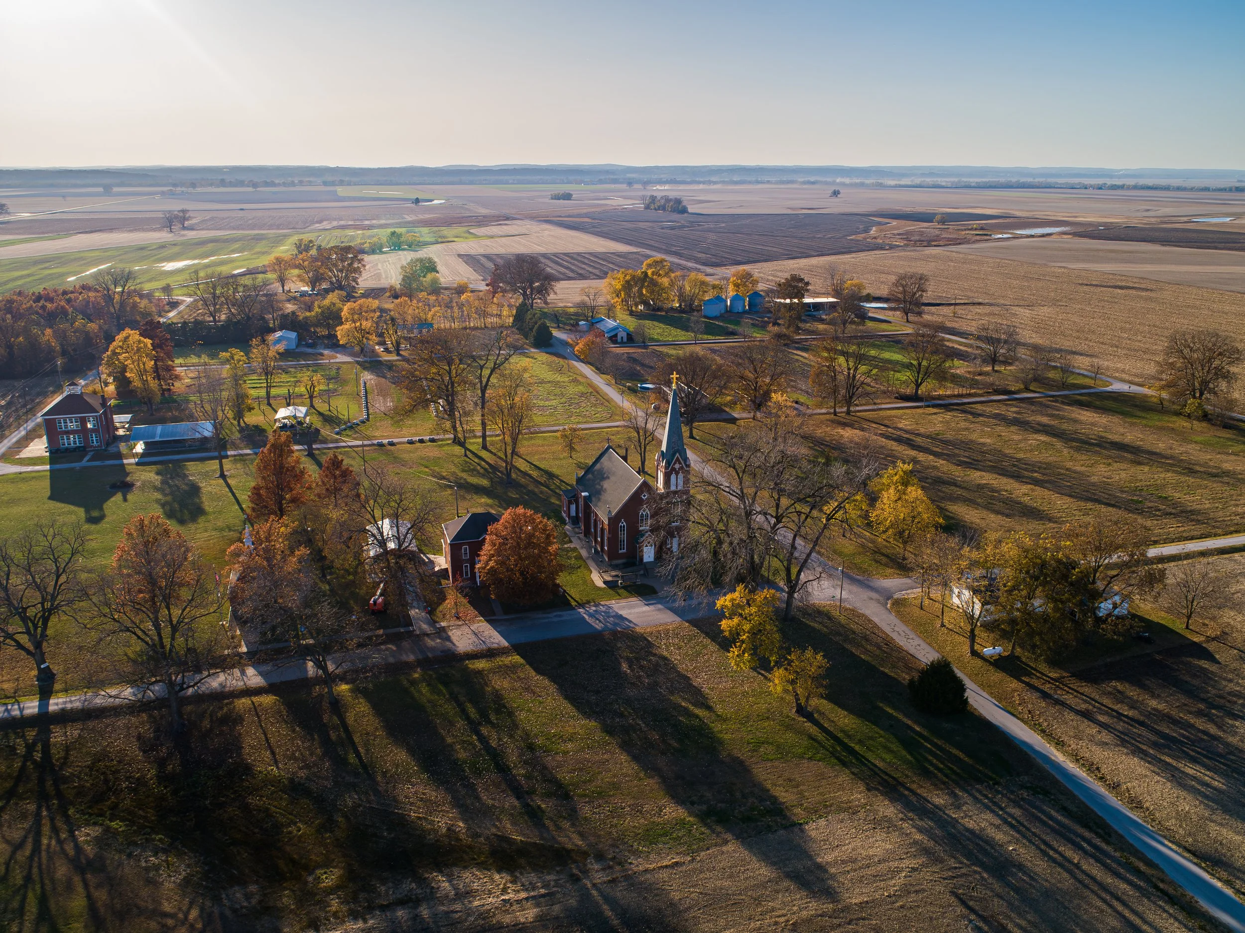Aerial view of a rural landscape with farmland, trees, a church with a steeple, and fields stretching to the horizon on a clear day.