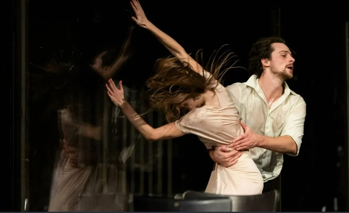 A dramatic scene with a man holding a woman against a glass surface in a theatrical performance.