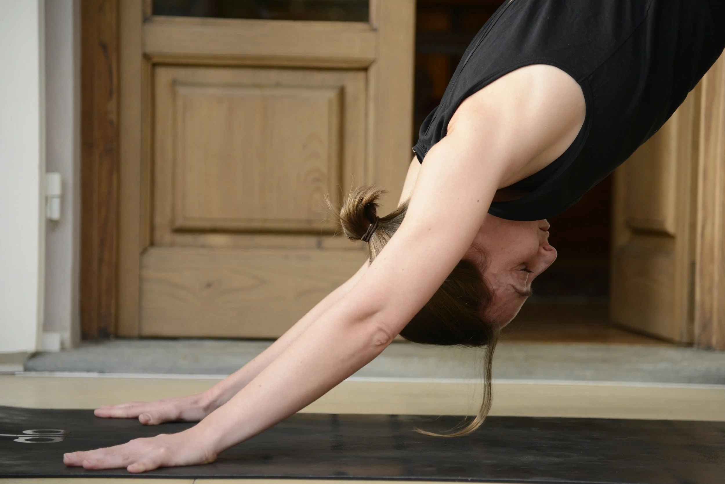 A woman practicing yoga in downward dog pose in a home setting with wooden doors in the background.
