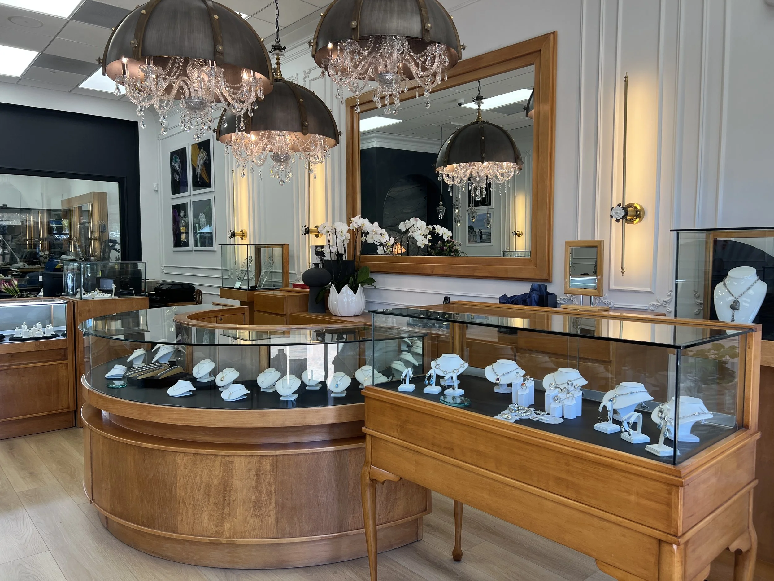 Jewelry showroom counter with curved glass display case, framed mirror and brass sconces
