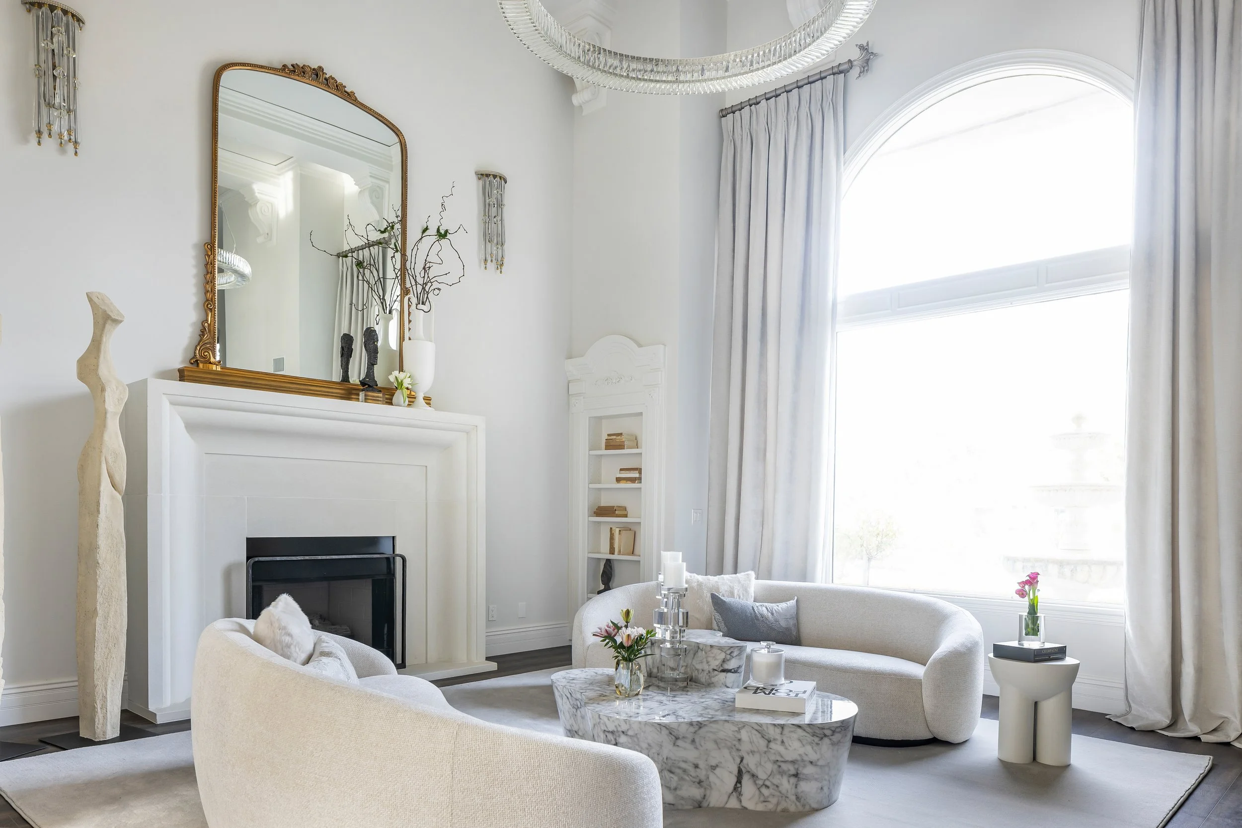 Living room with gold arched mirror over the fireplace and curved boucle sofa designed by LUXYSPACE, Mission Viejo interior designer