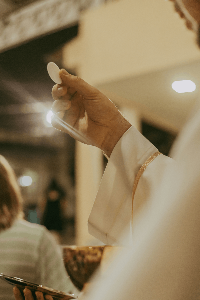Close-up of a priest's hand holding a wafer during communion in a church, with blurred background.