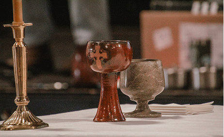 Two ornate goblets, one tall candlestick holder, and some plates and utensils on a table.
