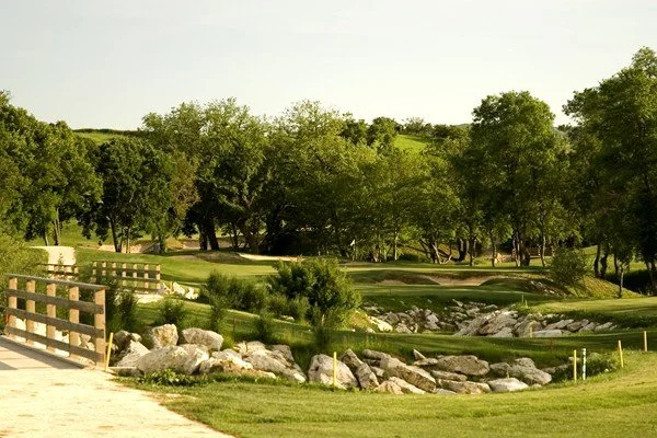 A scenic view of a golf course with trees, rocks, and a walking path under a clear sky.
