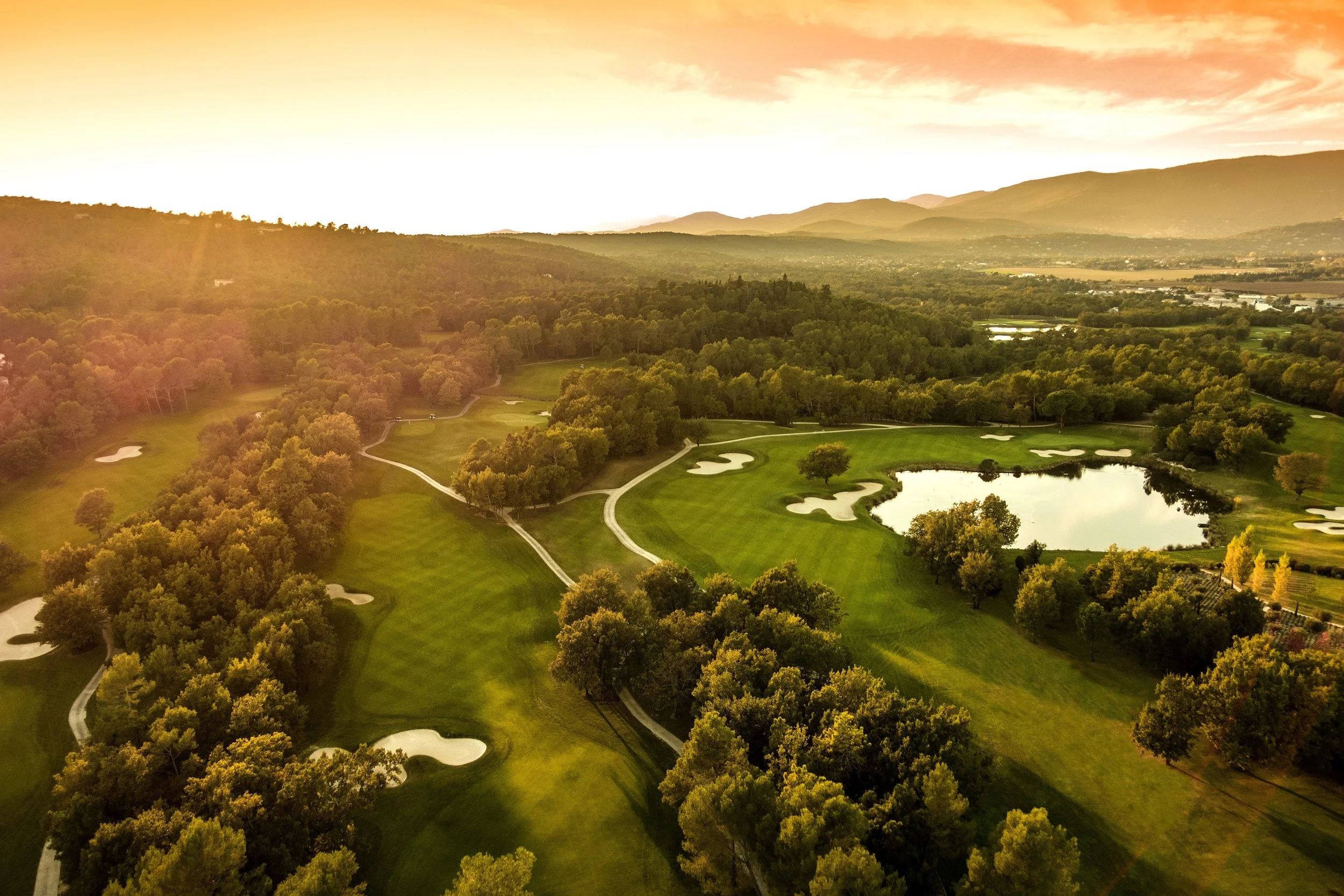 A golden aerial view of the sweeping fairways, white sand bunkers, and a calm lake at the Château course at Terre Blanche, the five-star destination for our VIP luxury ladies' golf retreats in Provence, France.