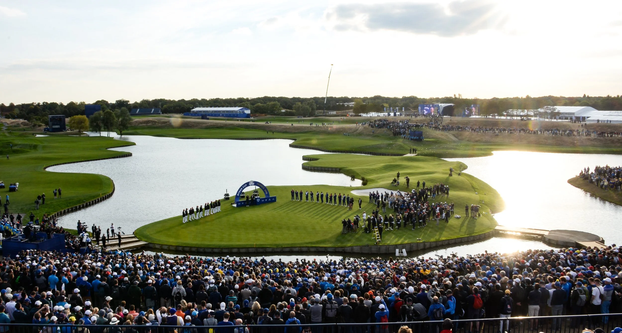 Players stand on the iconic island green surrounded by water and massive grandstands during the 2018 Ryder Cup at Le Golf National, a premier championship course featured in our luxury Paris golf itineraries.