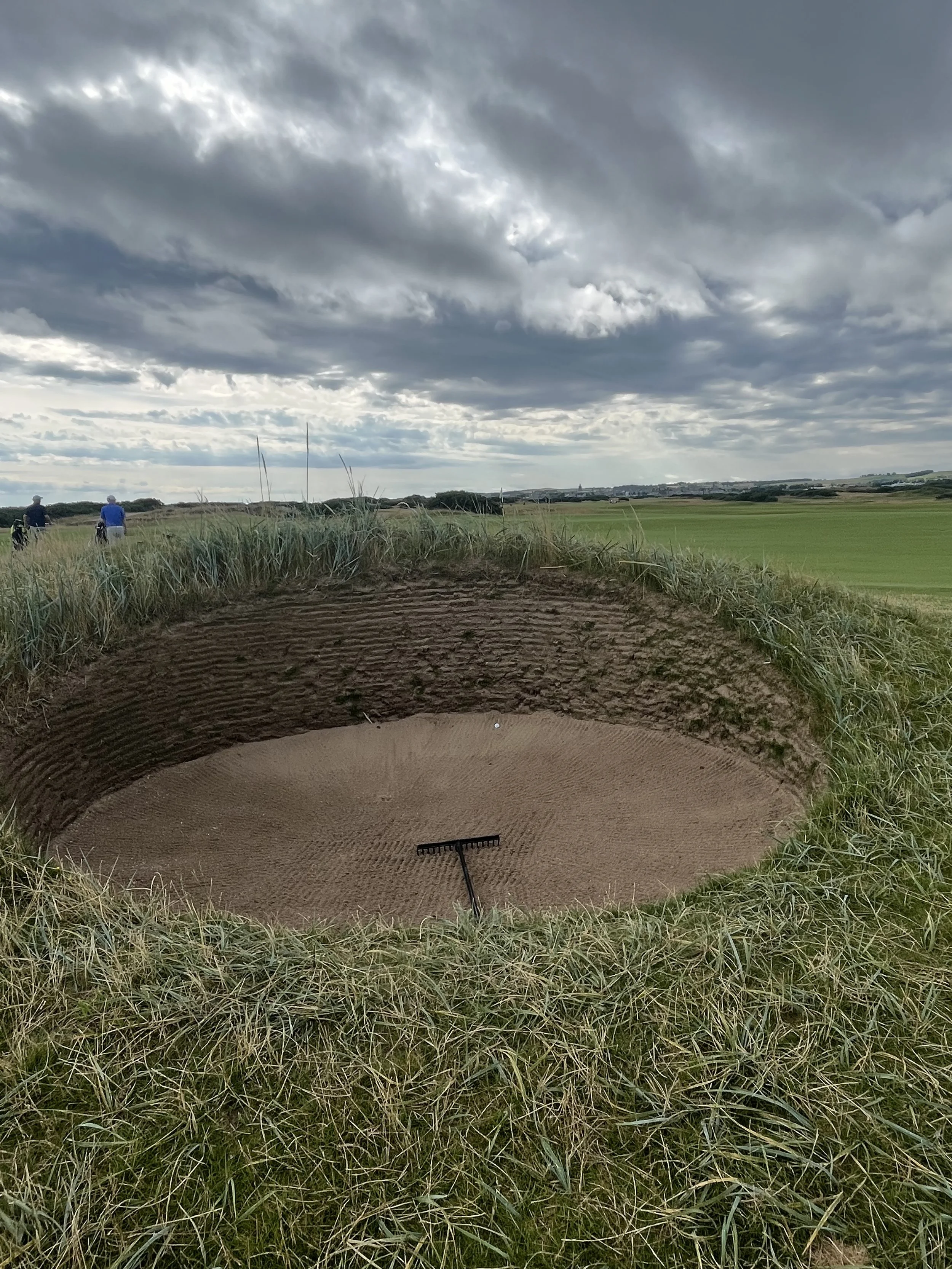A sand trap on a golf course with tall grass and cloudy skies.