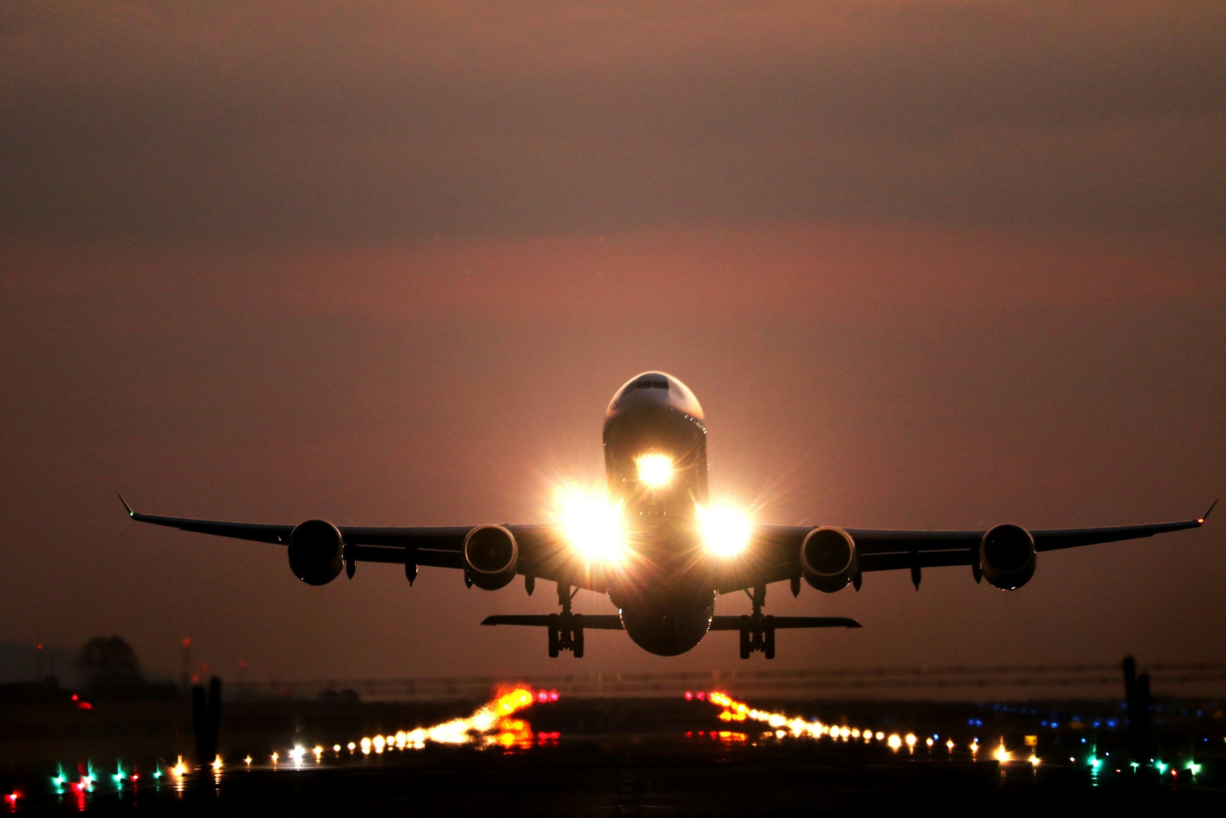 A large commercial airplane taking off on a runway with bright lights, during sunset or dusk.