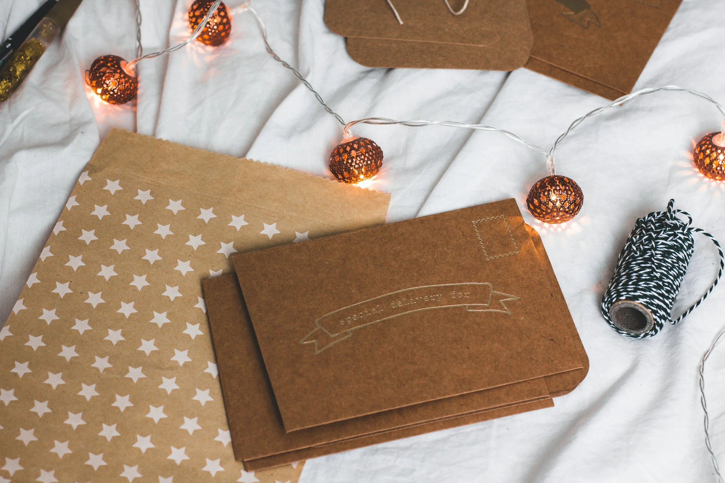 Brown paper envelopes and decorative string lights on a white fabric surface.