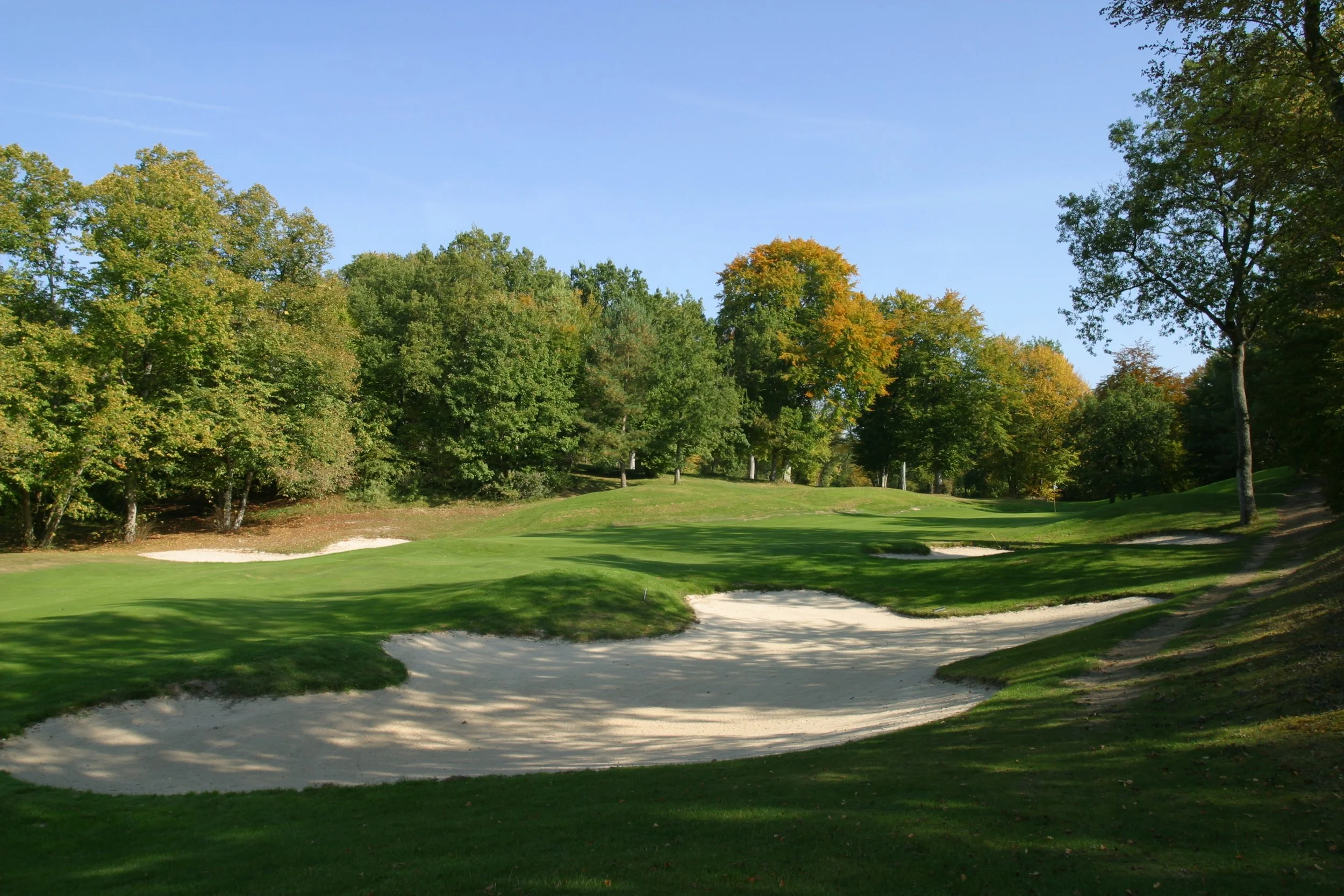 A golf course with sand bunkers, green grass, and trees in the background on a sunny day.