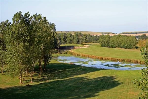 Scenic view of a golf course with a pond, surrounded by trees and open landscape under a clear sky.