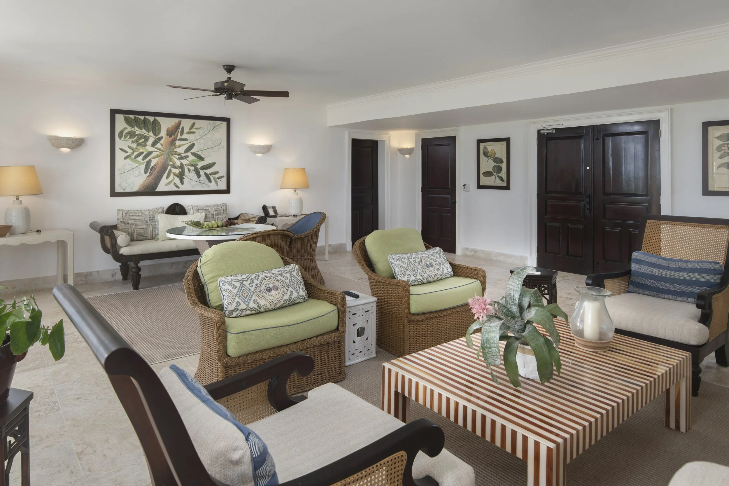 Living room with wicker and wood furniture, striped and solid cushions, framed botanical art, and a ceiling fan.