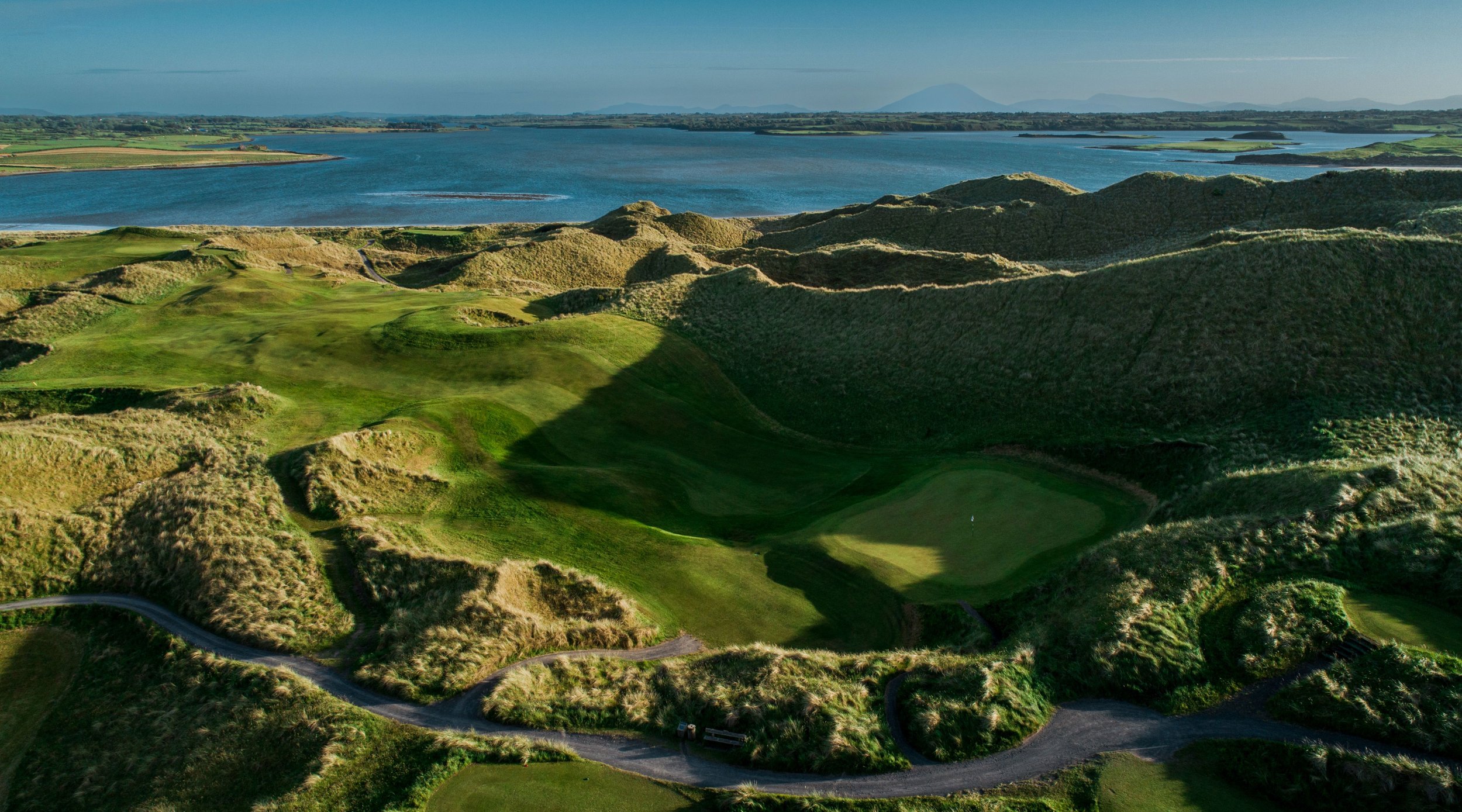 Dramatic towering dunes and a hidden green at Enniscrone Golf Club overlooking the water, highlighting the rugged and scenic links courses featured on premium golf in Ireland trips.