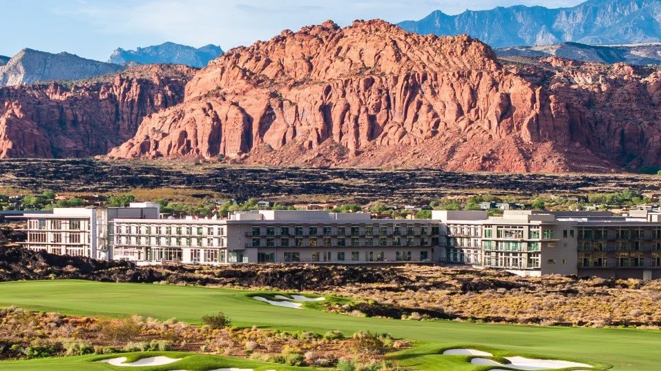 Resort hotel with golf course in the foreground and red rocky mountains in the background.