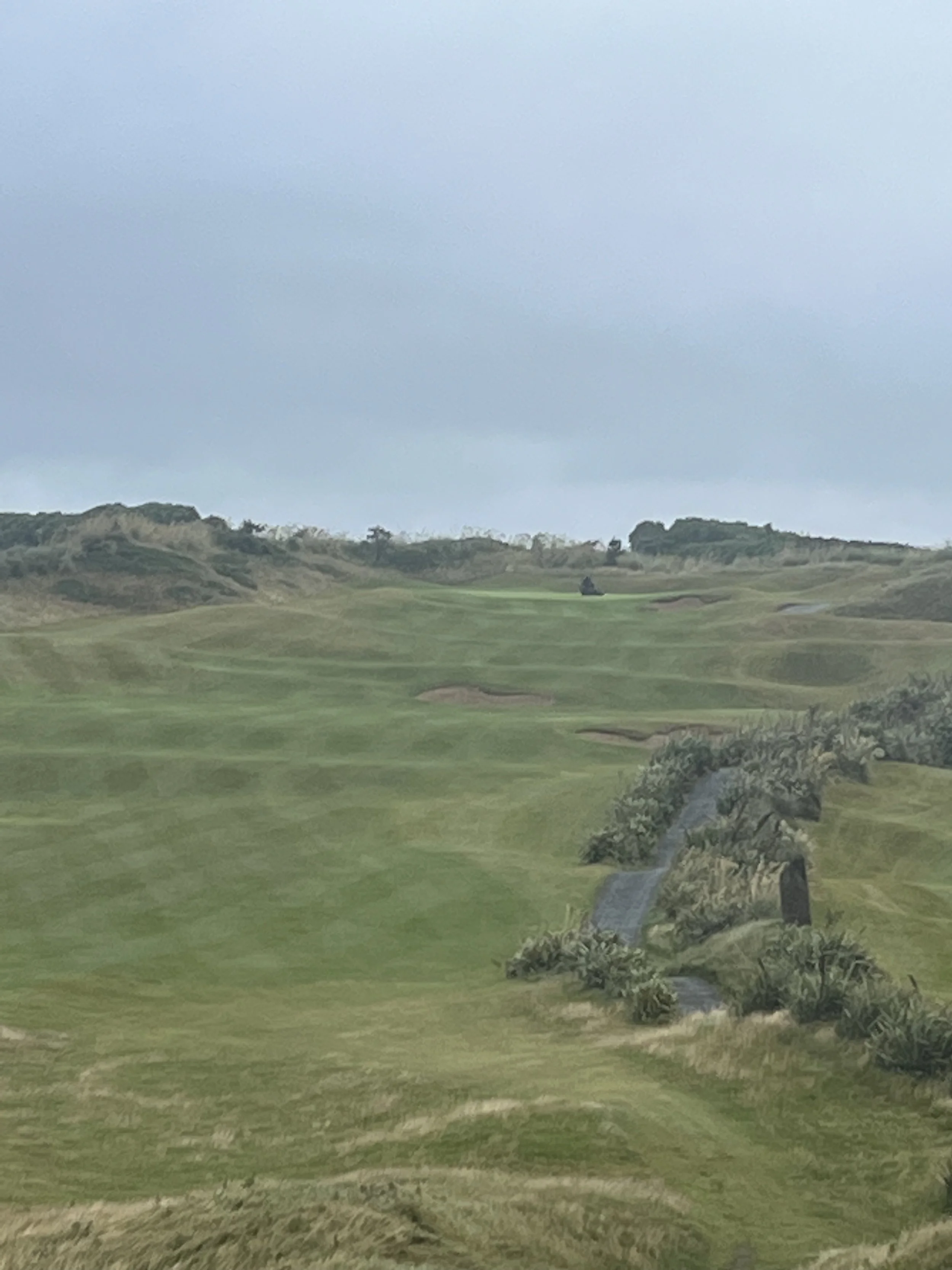 A scenic view of a golf course with green fairways, bunkers, and a small waterfall, under a cloudy sky.