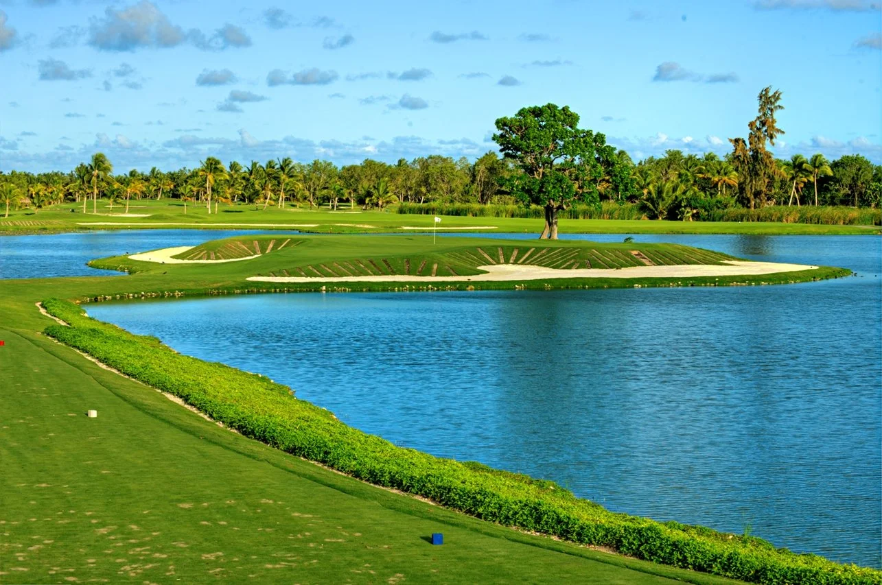 A golf course with water hazards, green fairways, and tall trees under a partly cloudy sky.