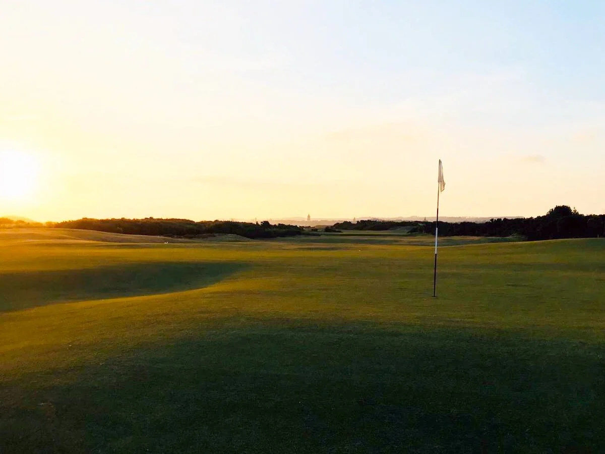 Golf course at sunset with a flagstick on the green, clear sky
