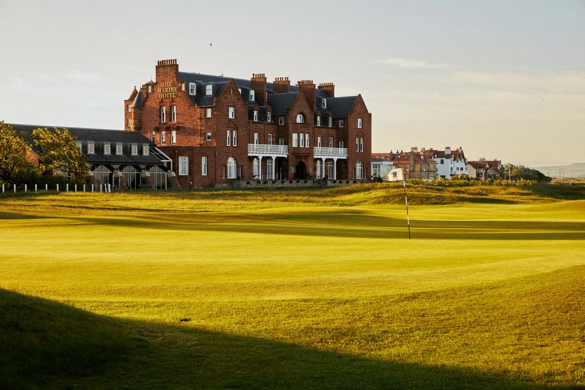 Exterior view of a large brick hotel surrounded by a golf course with a putting green and flagstick in the foreground.