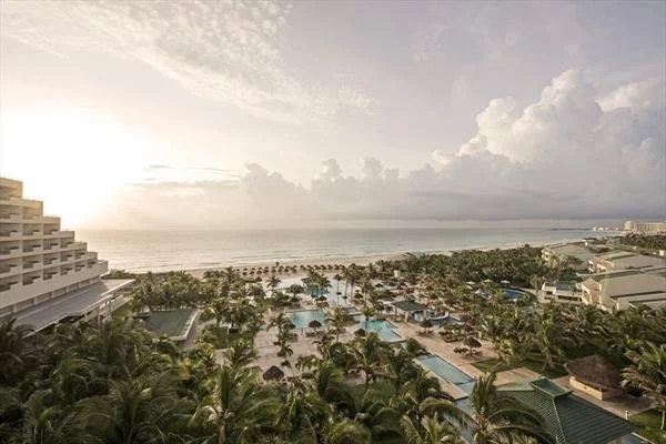 View of a beach resort with swimming pools, palm trees, and the ocean in the background during sunset.