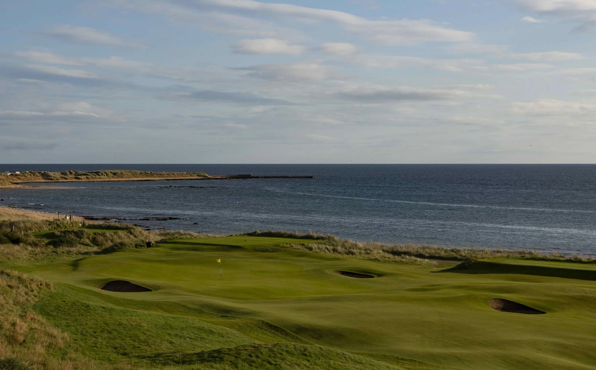 A golf course near the coast with green fairways, sand traps, and the ocean in the background.