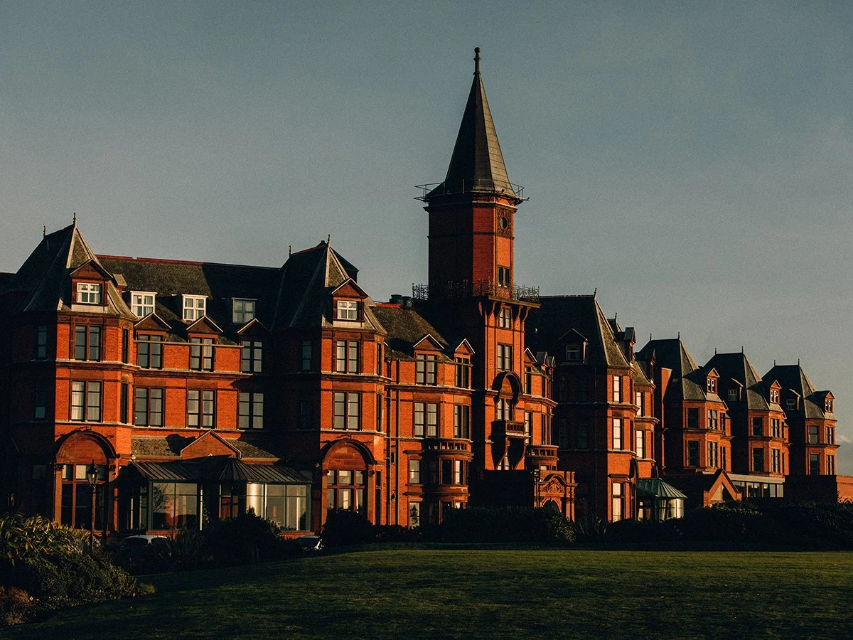 A large historic brick building with a prominent tower and multiple gabled roofs under a clear sky.