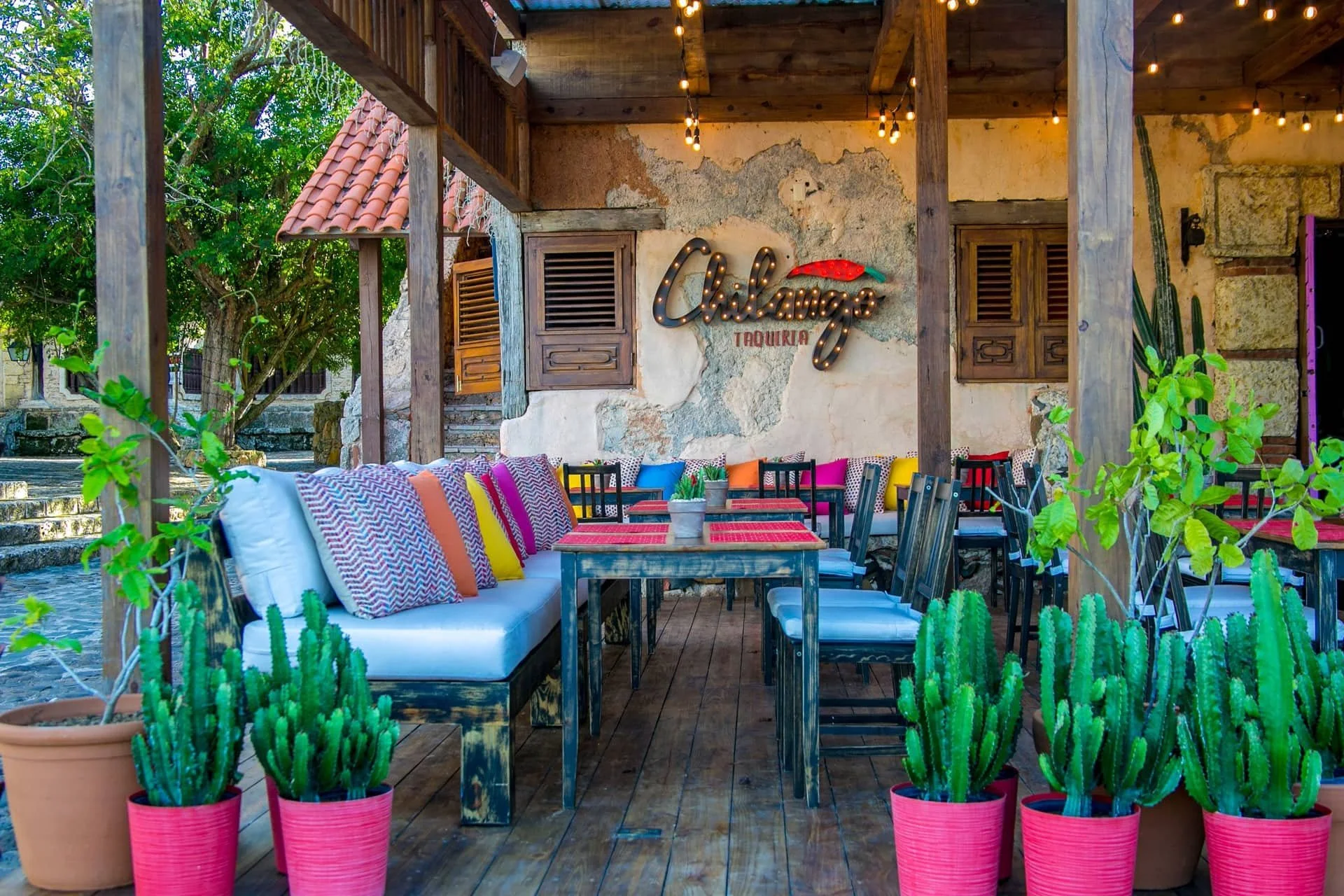 Outdoor patio with colorful seating, potted cacti, and a sign that reads 'Chilangos Taqueria' on a rustic wall.
