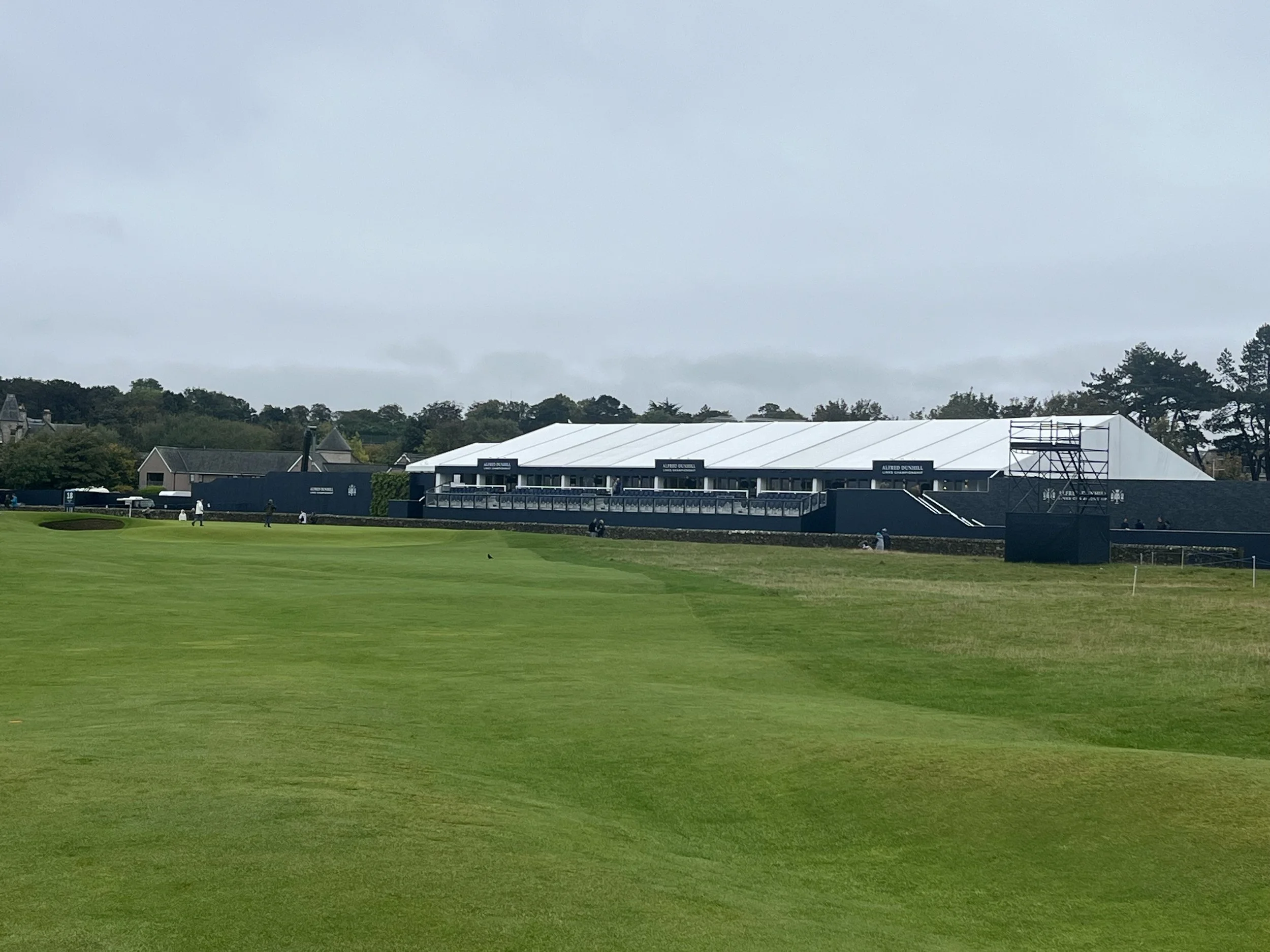 A wide view ot the famous 17th hole fairway at the St Andrews Old Course under an overcast sky,lined with a massive white hospitality tent for the Alfred Dunhill Links Championship, showcasing the world-class tournament atmosphere featured on our lux