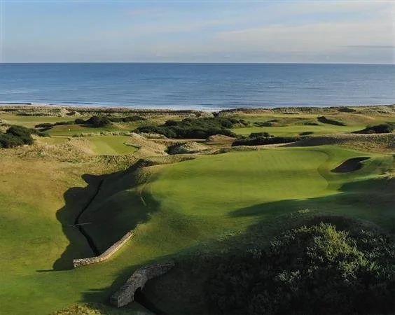 A golf course with green fairways and sand traps, overlooking the ocean on a clear day.