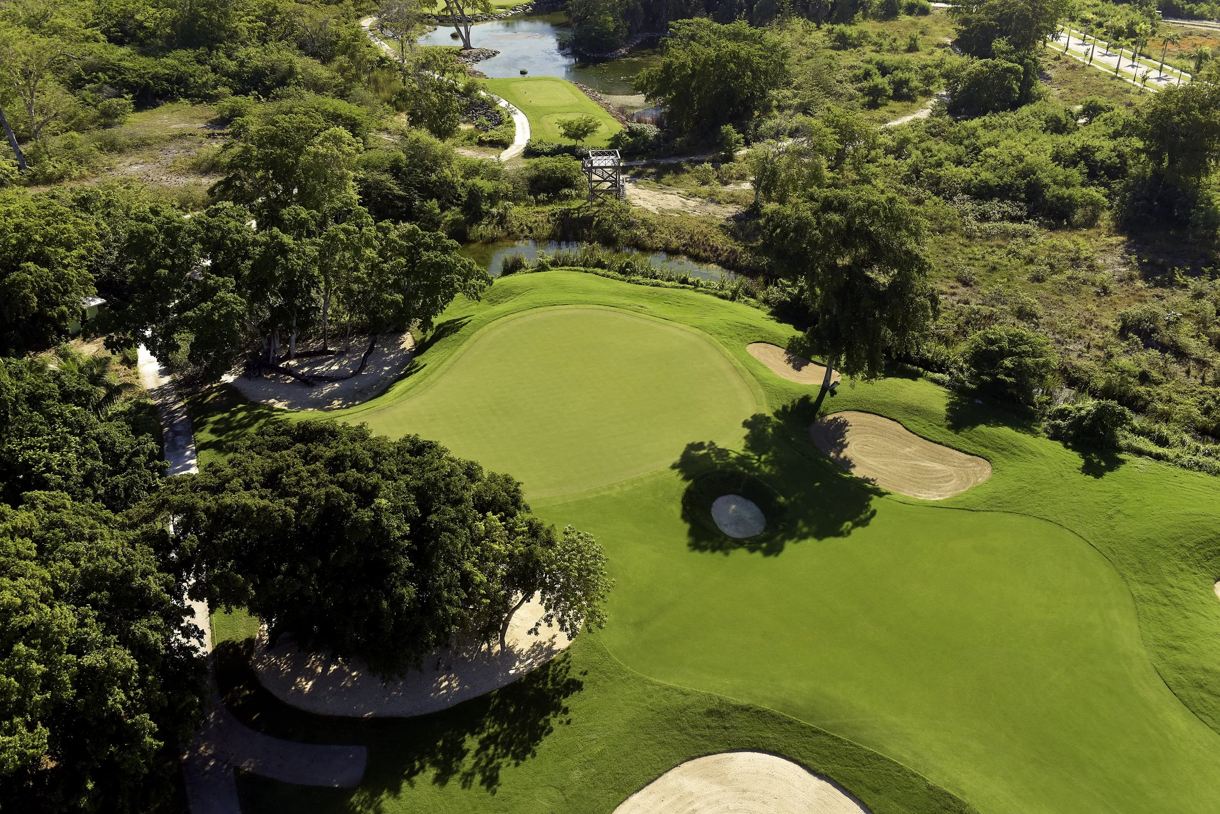 Aerial view of a golf course with green fairways, sand bunkers, water hazards, and surrounding trees.